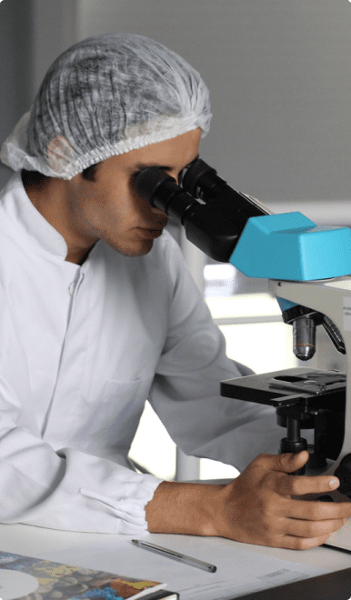 A man in white lab coat looking through microscope.