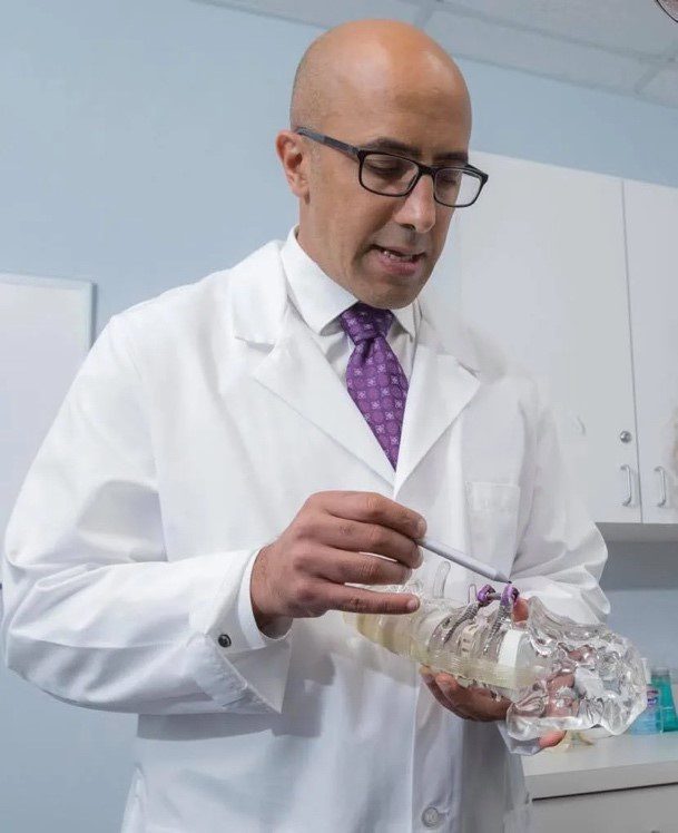 A man in white lab coat holding a wire.