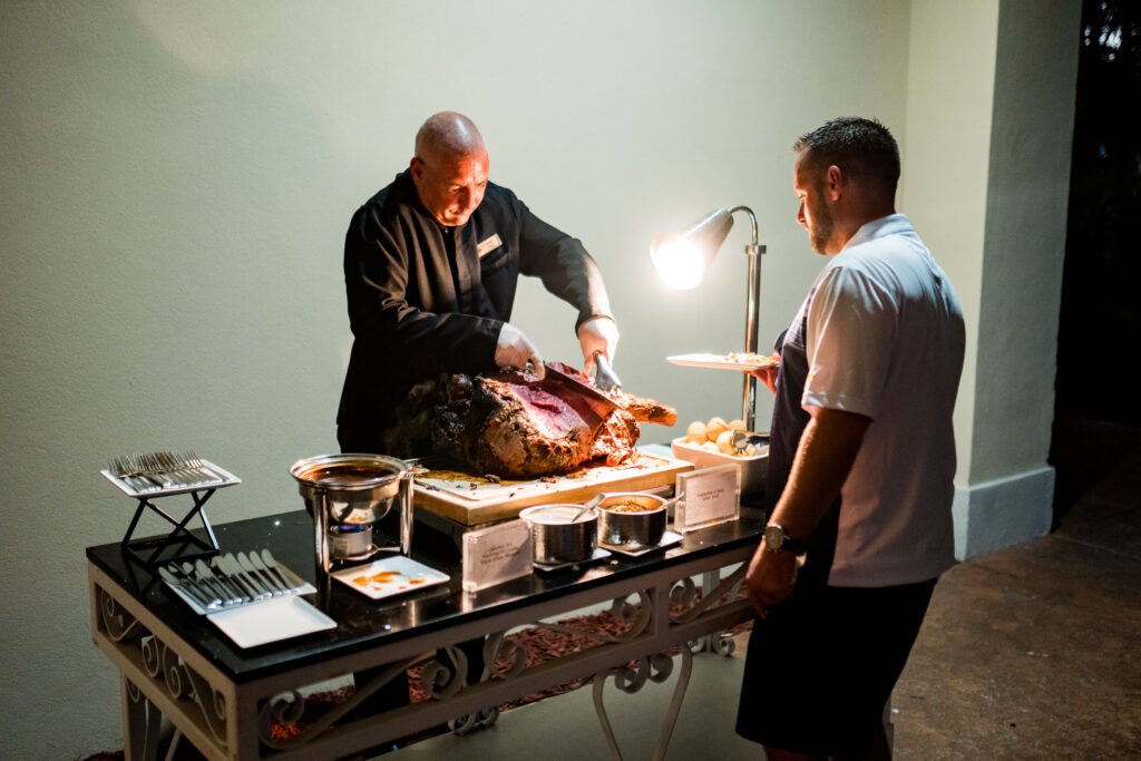 Two men standing around a table with food.