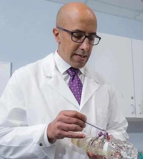 A man in white lab coat holding a pair of scissors.